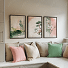 A cozy nook with pink, beige, and green cushions. Above, three framed art pieces from a Japandi Wall Art Set depict serene landscapes and florals, creating a tranquil ambiance.