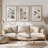 A cozy living room with a beige sofa and a round wooden coffee table. Three framed Zen Garden Prints depicting smooth stones on sand hang on the wall, adding a tranquil and minimalist touch.