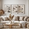 A cozy living room with a beige sofa adorned with neutral pillows. Above, three framed Zen Garden Prints featuring sand and stone patterns enhance the tranquil and minimalist decor.