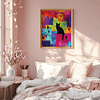 This cozy bedroom has pastel pink walls and soft sunlight streaming in. A Colorful Cat Art print of a black cat sitting on a vibrant, abstract cityscape hangs above a neatly made bed with patterned pillows. A vase with cherry blossoms and books sits on a light wooden nightstand.