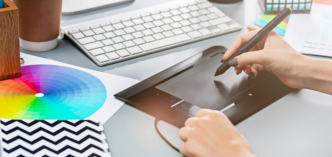 The desk with laptop, notepad with blank sheet, pot of flower, stylus and tablet for retouching. Workspace of professional retoucher. Creativity, design, art and modern equipments concept