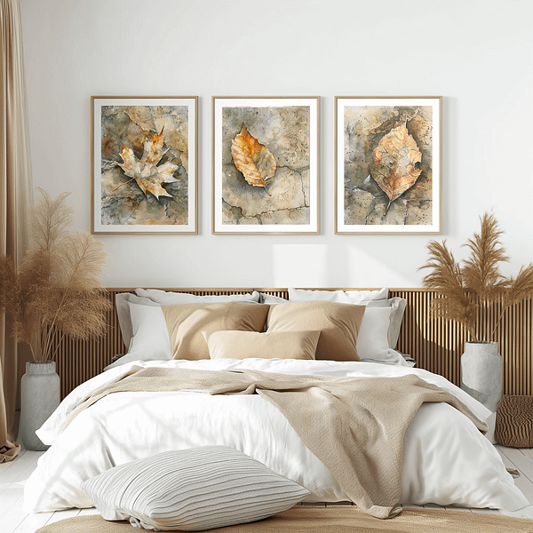 This minimalist bedroom features three wabi-sabi leaf art prints above a cozy bed. The artwork's earthy tones of beige, brown, and soft orange match the neutral bedding and pampas grass decor, creating a peaceful and harmonious ambiance.