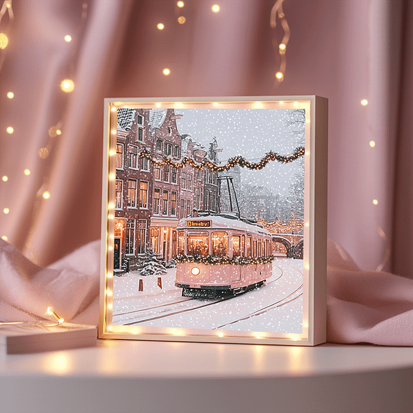 This framed Christmas tram artwork features warm, glowing fairy lights against a pastel pink curtain for an elegant holiday vibe.